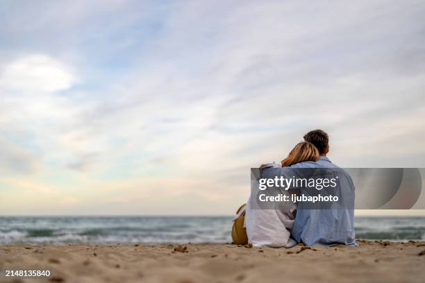 couple looking to the horizon at the shore - human made stock pictures, royalty-free photos & images