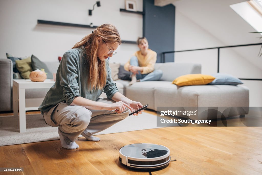 Frau schaltet Roboterstaubsauger ein