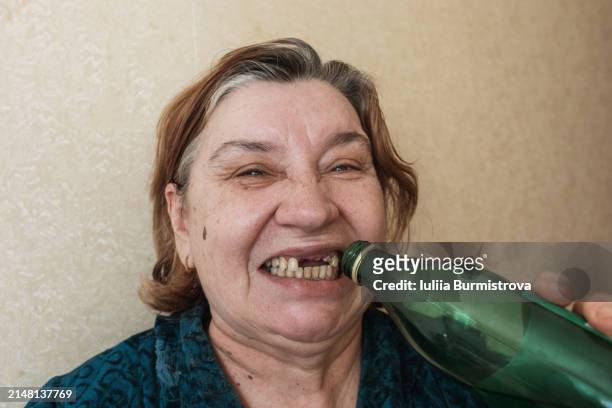 toothless adult homeless woman opens a metal bottle cap with her teeth - gingivitis stock-fotos und bilder