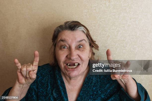 the toothless adult homeless woman shows the rock on gesture with her hands. - gingivitis stock-fotos und bilder