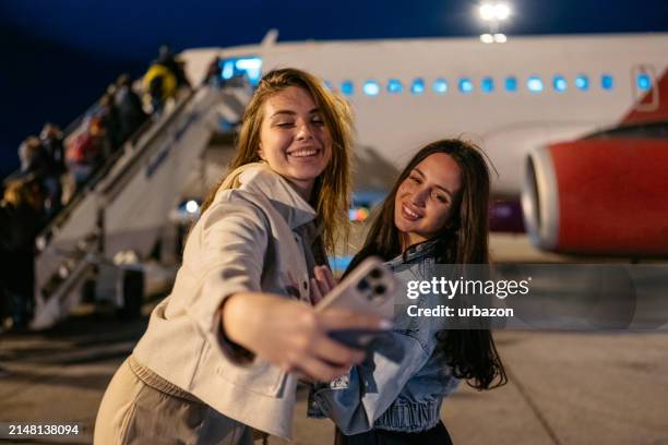 zwei freundinnen machen selfies, während sie nachts in ein flugzeug steigen - flugpassagier stock-fotos und bilder