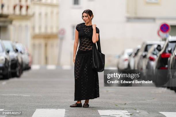 Katie Giorgadze wears earrings, a black drop waist crochet mesh dress by Jil Sander, black bras and underwear, an oversized big black tote leather...