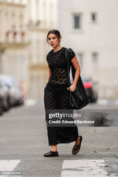 Katie Giorgadze wears earrings, a black drop waist crochet mesh dress by Jil Sander, black bras and underwear, an oversized big black tote leather...
