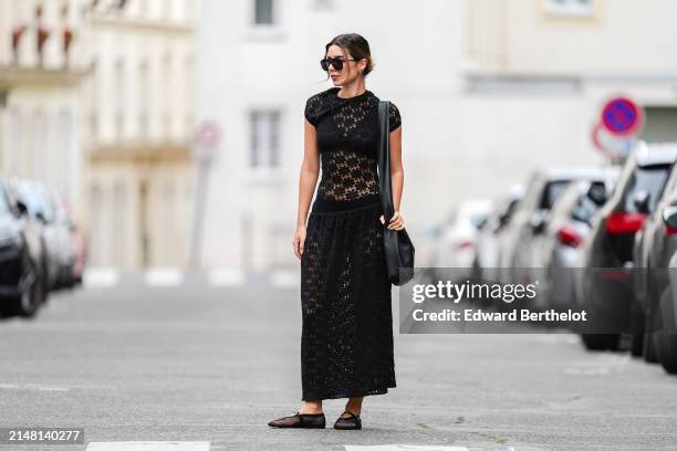 Katie Giorgadze wears sunglasses, earrings, a black drop waist crochet mesh dress by Jil Sander, black bras and underwear, an oversized big black...