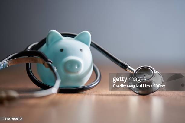 close-up of piggy bank with stethoscope on table - medical savings stock pictures, royalty-free photos & images