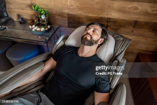 mid adult man sleeping on a massage chair at home - massage chair stock pictures, royalty-free photos & images