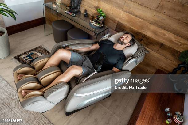 mittlerer erwachsener mann, der zu hause auf einem massagesessel schläft - massagestuhl stock-fotos und bilder