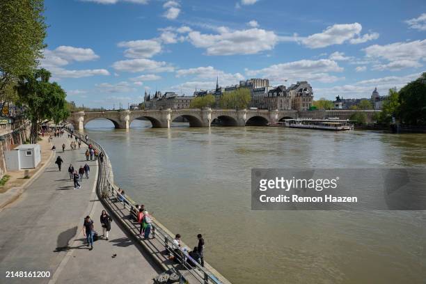 People are seen relaxing next to the river Seine with the Pont Neuf in the background on April 10, 2024 in Paris, France. Since September 2023 the...