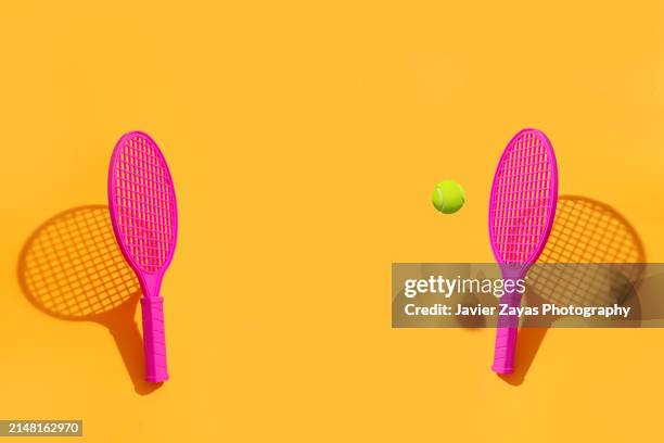 two magenta tennis rackets and ball on yellow colored background - handle stock-fotos und bilder