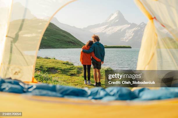 man and woman camping near the lake in swiss alps with the tent - zwitserse alpen stockfoto's en -beelden
