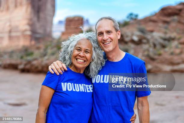 una pareja birracial sonríe a la cámara mientras se ofrece como voluntaria en un evento al aire libre - voluntario fotografías e imágenes de stock