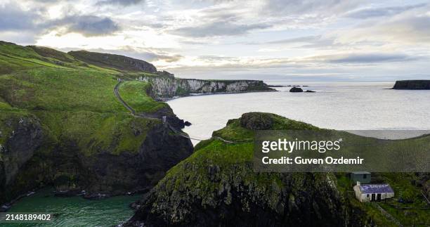 aerial view of two islands with carrick-a-rede rope bridge in northern ireland, carrick-a-rede rope bridge connecting two islands in ireland, rope bridge connecting two cliffs in northern ireland, carrick-a-rede rope bridge - hanging bridge stock pictures, royalty-free photos & images
