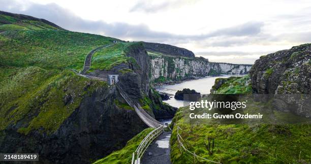 aerial view of two islands with carrick-a-rede rope bridge in northern ireland, carrick-a-rede rope bridge connecting two islands in ireland, rope bridge connecting two cliffs in northern ireland, carrick-a-rede rope bridge - hanging bridge stock pictures, royalty-free photos & images