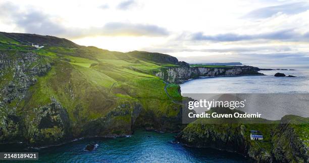 aerial view of two islands with carrick-a-rede rope bridge in northern ireland, carrick-a-rede rope bridge connecting two islands in ireland, rope bridge connecting two cliffs in northern ireland, carrick-a-rede rope bridge - carrick a rede stock pictures, royalty-free photos & images