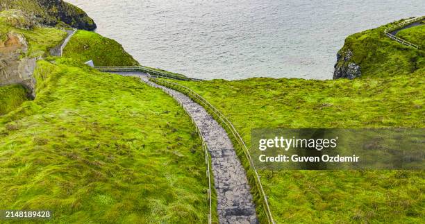 aerial view of two islands with carrick-a-rede rope bridge in northern ireland, carrick-a-rede rope bridge connecting two islands in ireland, rope bridge connecting two cliffs in northern ireland, carrick-a-rede rope bridge - hanging bridge stock pictures, royalty-free photos & images