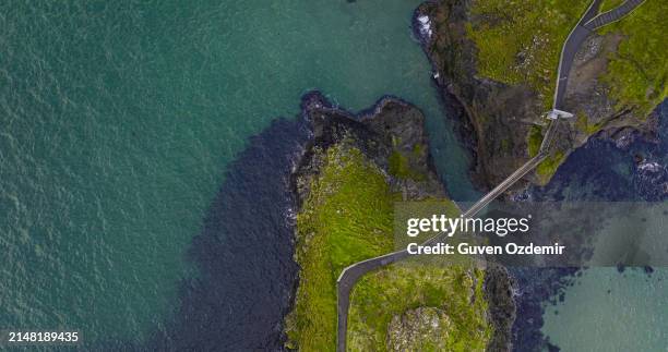 aerial view of two islands with carrick-a-rede rope bridge in northern ireland, carrick-a-rede rope bridge connecting two islands in ireland, rope bridge connecting two cliffs in northern ireland, carrick-a-rede rope bridge - hanging bridge stock pictures, royalty-free photos & images