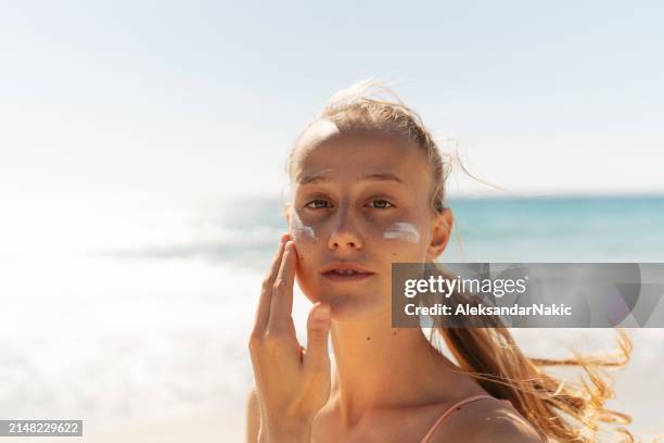 young woman applying sunscreen on her face while at the beach - blonde hair on tan skin stock pictures, royalty-free photos & images