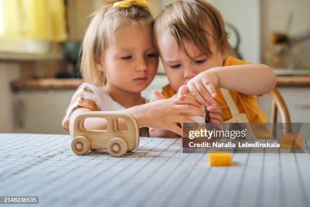 adorable siblings enjoying eco-friendly wooden toys, playing together at kitchen table, safe and sustainable playtime. - family with two children stock pictures, royalty-free photos & images