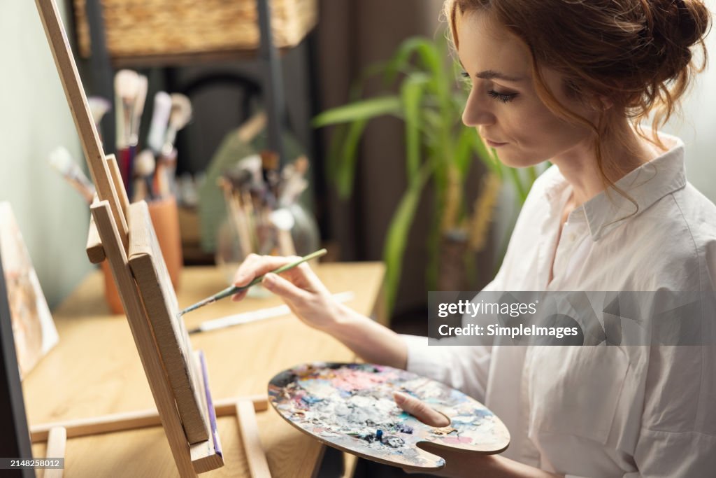 Beautiful female painter enjoying while painting in home art studio. Woman Artist Works on Abstract acrylic painting in the art studio.