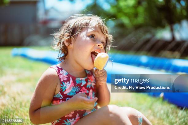 toddler girl wearing swimsuit eating popsicle in back yard - hot american girl stock pictures, royalty-free photos & images