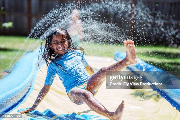 indian girl having fun playing on slip n slide - water slide grass stock pictures, royalty-free photos & images