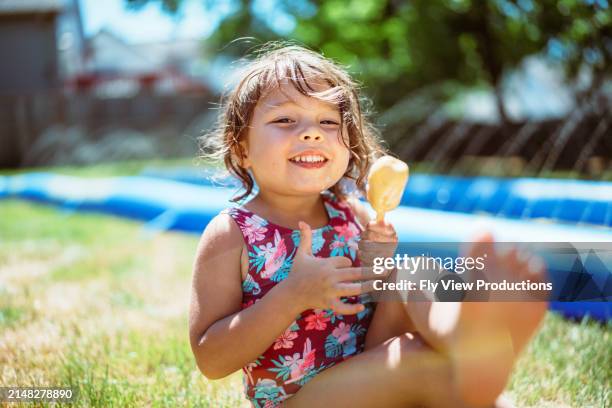 girl smiles while eating a popsicle in her backyard - hot american girl stock pictures, royalty-free photos & images