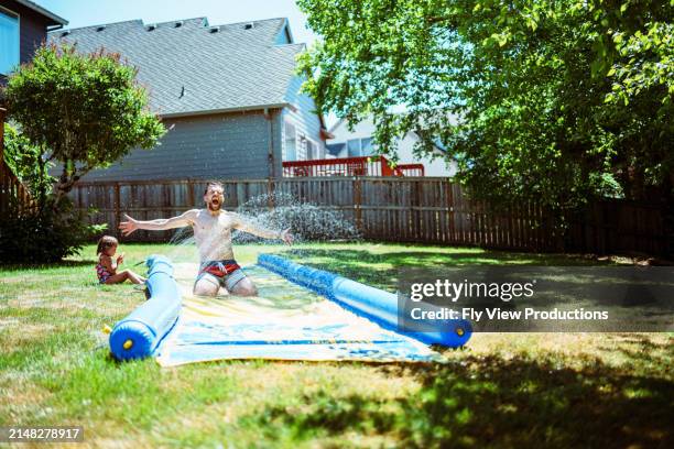 man having fun on slip n slide while playing outside with his daughter - sliding stock pictures, royalty-free photos & images