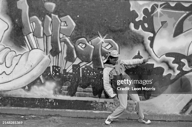 Hip hop dance instructor and breakdancer against a graffiti backdrop reading 'Hip Hop', London, 1985.