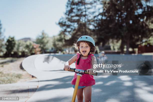 happy eurasian girl riding her scooter at a skate park - push scooter stock pictures, royalty-free photos & images