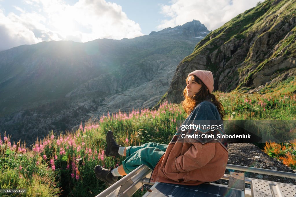 Woman sitting on rooftop of camper van overlooking Furka Pass