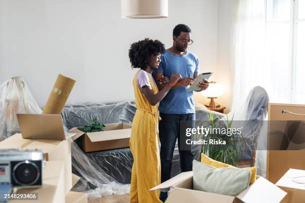ein junges paar zieht ein. sie verwenden tablets - wohngebäudeversicherung stock-fotos und bilder