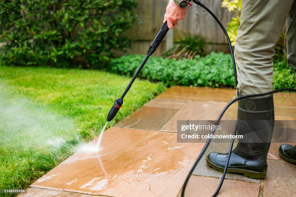Senior man cleaning patio tiles using pressure washer