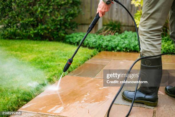 senior man cleaning patio tiles using pressure washer - garden machinery stock pictures, royalty-free photos & images