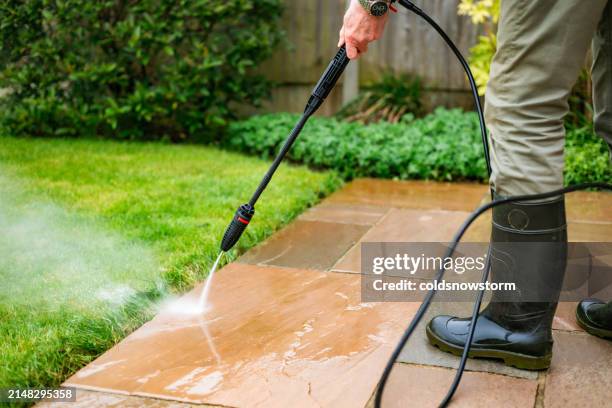 senior man cleaning patio tiles using pressure washer - paving stone stock pictures, royalty-free photos & images