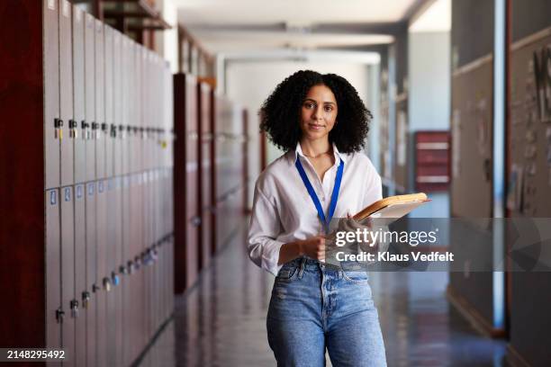 confident teacher standing with file folder in corridor - équipement à base de papier photos et images de collection