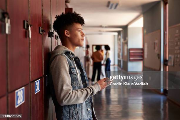 thoughtful teenage boy leaning on lockers in corridor - student profile pic stock pictures, royalty-free photos & images