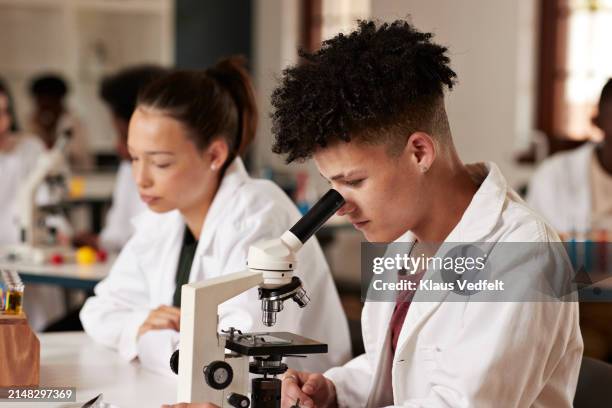teenage boy looking through microscope female friend - optical character recognition stock pictures, royalty-free photos & images