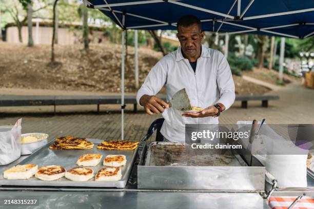 afro-descendant man serves cheese arepa at street stall. - mercado colombia fotografías e imágenes de stock