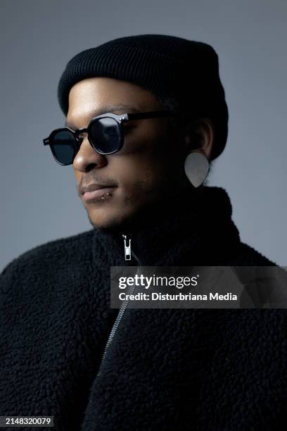african-american male with black-framed tinted glasses, all black clothing, and left lip-piercing; looking away; jacket zippered up - blixtlås bildbanksfoton och bilder