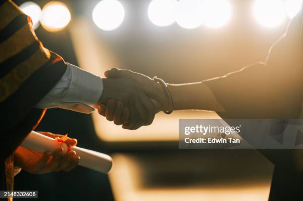 primer plano ceremonia de convocatoria asiático decano apretón de manos graduación estudiante universitario entrega pergamino de graduación en el escenario del auditorio - diploma fotografías e imágenes de stock