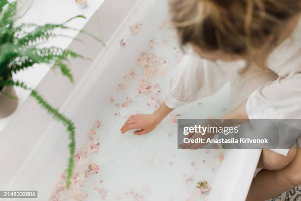 close up of womans hands in white bath with milk and rose petals. - white rose flower spa stock-fotos und bilder