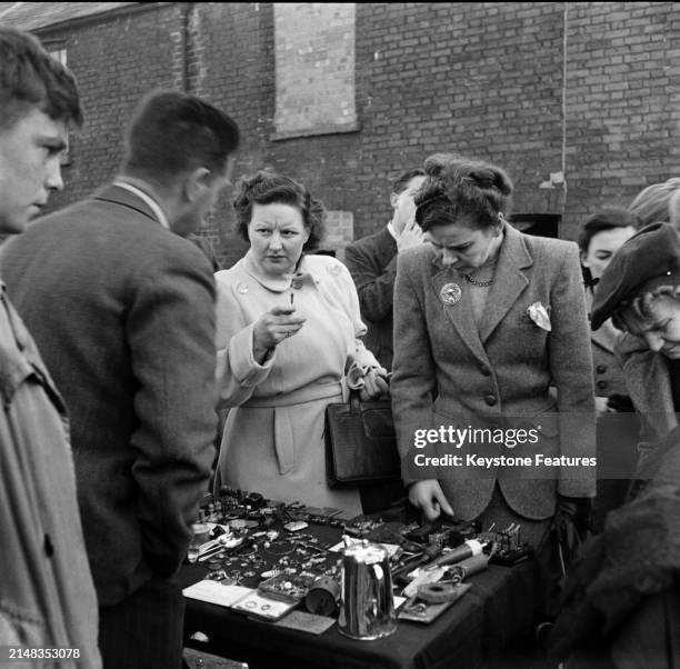 One woman speaks to the stallholder as another woman browses the wares on sale on a stall in The Lanes, shopping thoroughfares in Brighton, East...