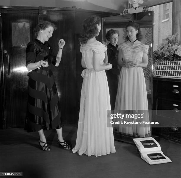 Dressmaker inspects a young woman who looks at her reflection in a full-length mirror in the Moss Bros shop in Covent Garden, in the West End of...