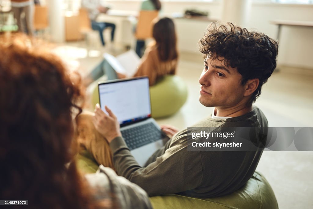 Male student talking to his friend while e-learning at casual classroom.