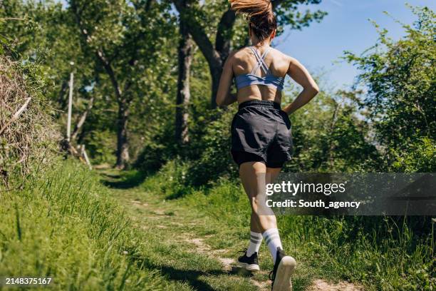 mid adult woman running in the forest on a sunny day - calções de corrida imagens e fotografias de stock