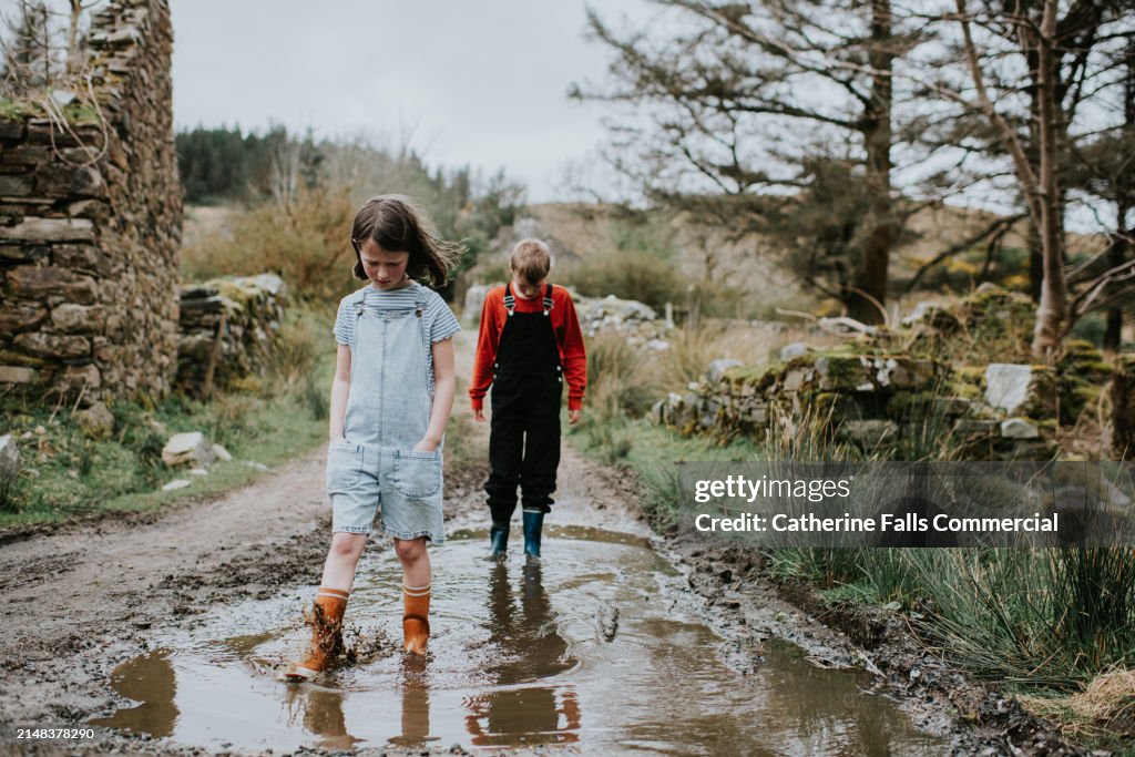 Children wearing wellington boots wade through a muddy puddle