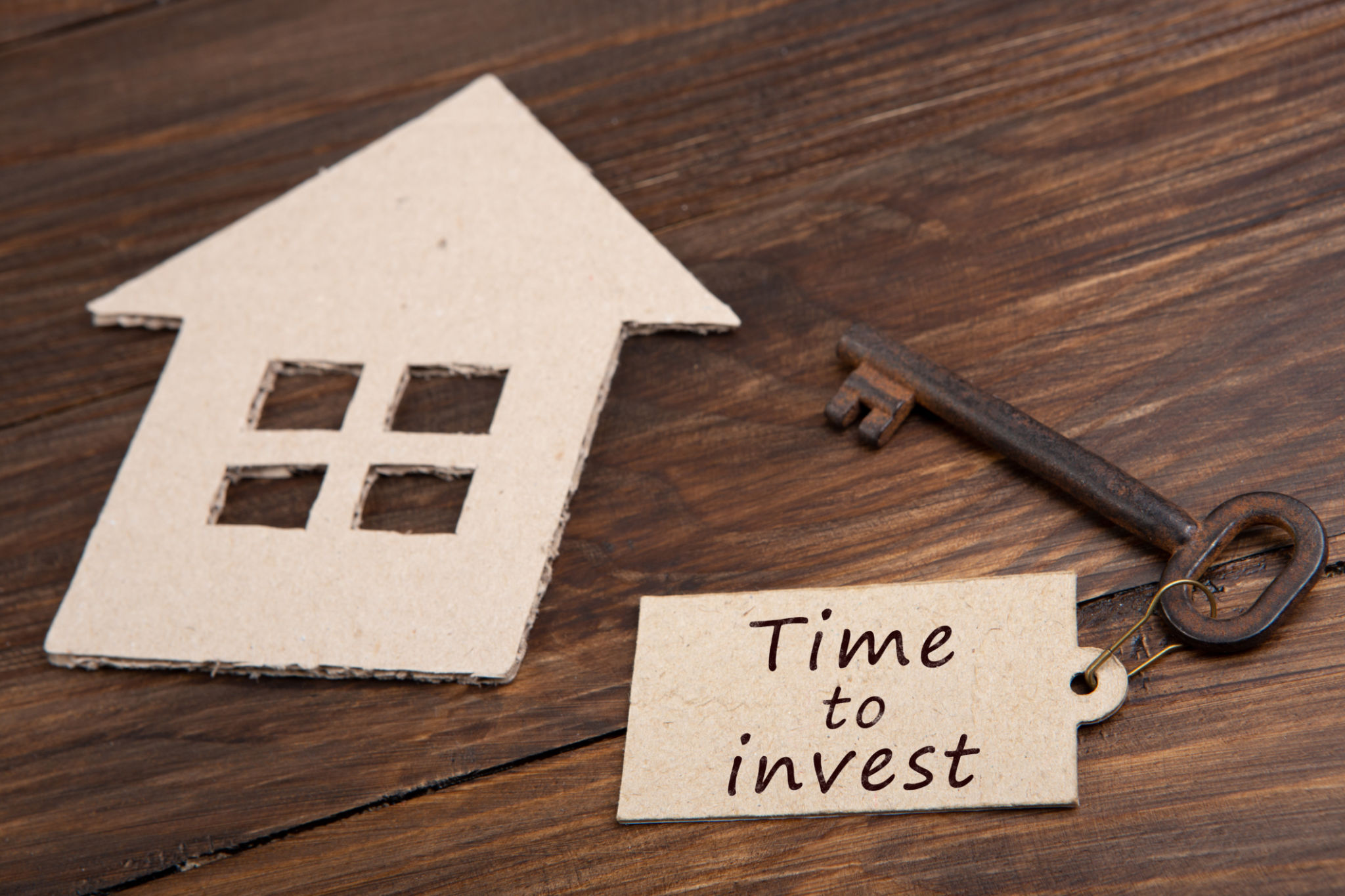 Time to invest - text on the key label. House model and old key on wooden background real estate buy or rent concept Time to invest - text on the key label. House model and old key on wooden background real estate buy or rent concept