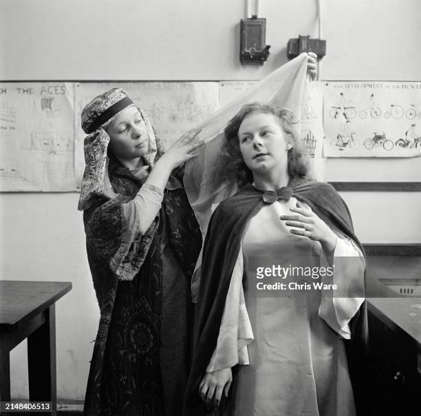 Schoolgirl Joan Adams, in costume as Joseph, helping schoolgirl Christine Statham with her headdress as they prepare for a performance of the...