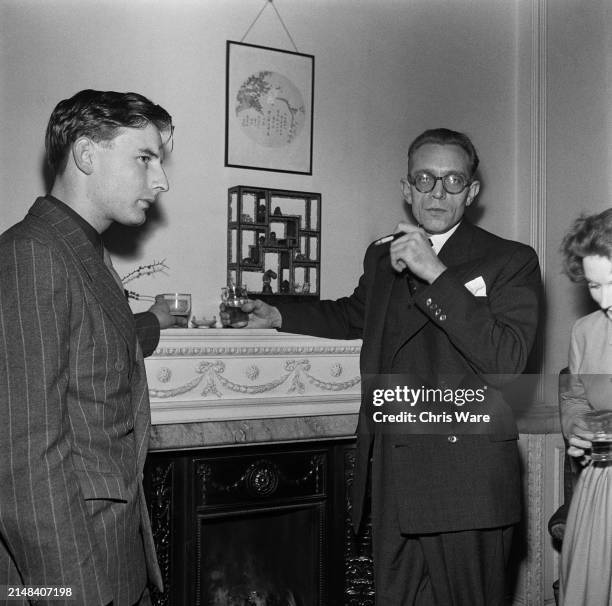 British film studio executive Alan Arnold, Pinewood Studios' Director of Publicity, in conversation beside a fireplace with British poet Howard...