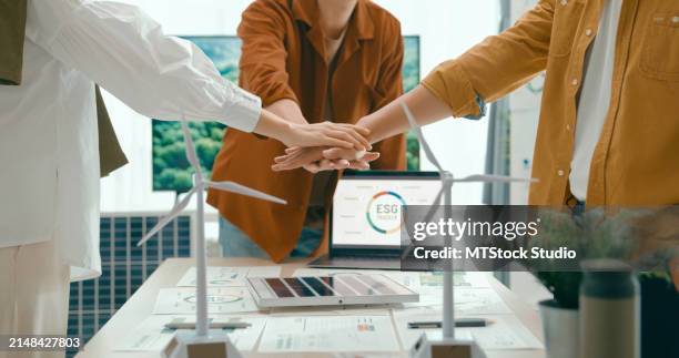 vielfältiges team vereint hände über schreibtisch mit modellen für erneuerbare energien und symbolisiert zusammenarbeit und vereinbarung nachhaltiger geschäftspraktiken. umweltfreundliches business-team diskutiert esg-ziele. - ethik und moral stock-fotos und bilder